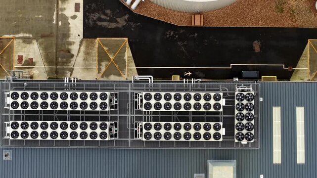 Top-down aerial drone view of industrial HVAC cooling units and ventilation fans atop a massive greenhouse facility in Cambridgeshire, UK.