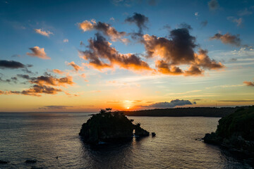 Glowing orange sunset illuminating clouds over a small tropical rock island in the sea