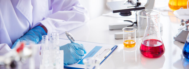 Fototapeta premium Banner Asian woman scientist hand write note research in medical lab look at science microscope. Asian Female technician laboratory using microscope with copy space. Banner Scientist chemistry