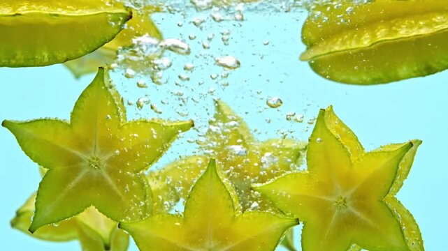 Bright yellow starfruit slices splashing into crystal clear water with refreshing bubbles