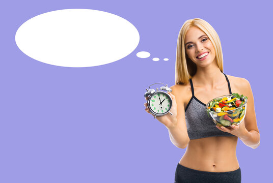 Plan meals, diet, healthy eat, intermittent fasting - concept. Happy smile woman wear sportswear holds bowl of salad, shows points alarm clock, isolated purple background. White thought speech bubble