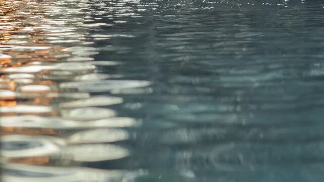 Sunlight reflections shimmer across moving water surface forming dynamic sparkling patterns that shift with small ripples and waves across the pool. Water reflections, abstract background.