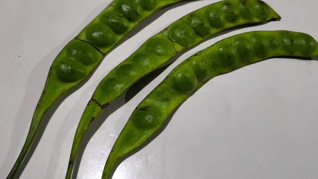 Fresh green petai pods displaying natural texture, curved shape, and visible bean segments clearly