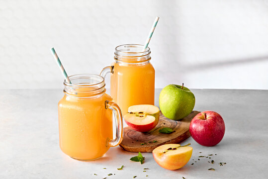 Fresh Apple Juice in Jam Jar Glasses with Straws and Fresh Apples on Wooden Board on Kitchen Counter 