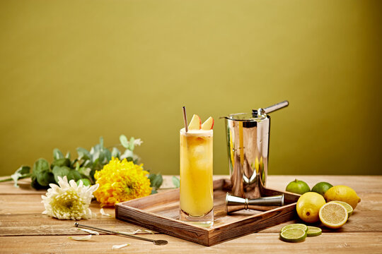 Yellow Summer Cocktail with Lemons and Limes in Tall Glass with Bar Tools on Wooden Tray