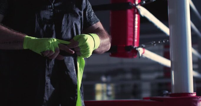 Watch a focused male fighter carefully wrap his hands with green bandages, emphasizing the importance of protection and stability before stepping into rigorous training or competition.