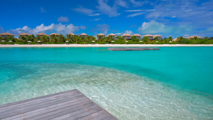 Fototapeta premium View from a wooden deck looking out over crystal clear turquoise water towards a row of beach villas on a tropical island