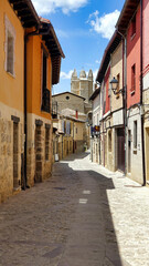 Obraz premium Castrojeriz, Spain, 21/05/2018 Description: Picturesque narrow street with stone houses and church tower in Castrojeriz