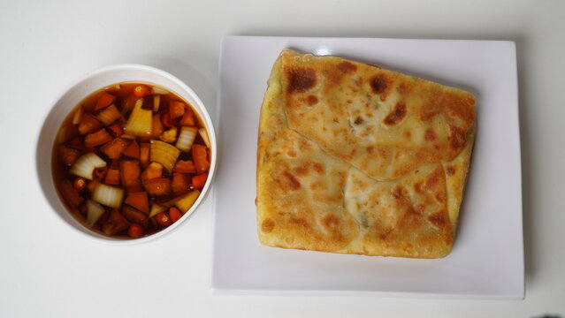 Martabak telur or martabak kubang served on a white plate with a bowl of pickled vegetables. This popular Indonesian street food.