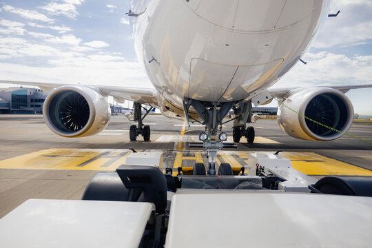 View from pushback tug towing passenger airplane away from airport terminal to taxiway. Ground handling operation, aviation logistics, airport operations, and aircraft departure concept.