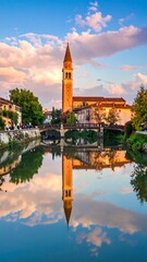 Obraz premium Scenic canal with towering spire reflecting in tranquil water at sunset, bright sky