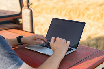 Farmer works on laptop next to an agricultural tractor. © scharfsinn86