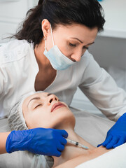 Woman beautician injecting rejuvenating filler into the neck of a female patient in a beauty clinic, close-up