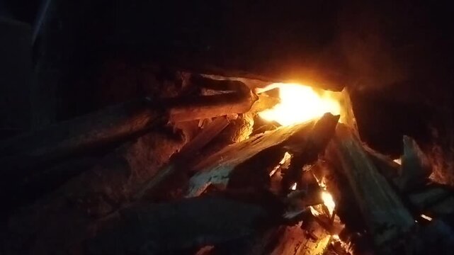 Close up video of burning firewood with bright orange flames in a dark environment. Natural wood fire producing warm light and glowing embers, creating a dramatic night atmosphere often associated wit