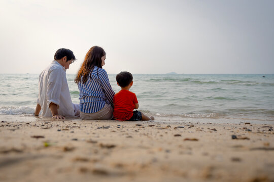 Happy Asian family with a young son enjoying sunset on the beach, playing in the sand and walking together during summer vacation.
