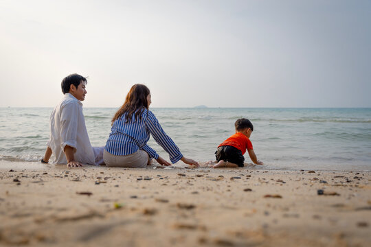 Happy Asian family with a young son enjoying sunset on the beach, playing in the sand and walking together during summer vacation.