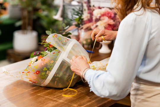 Florist arranging bouquet in flower shop, wrapping with floral cellophane and yellow ribbon