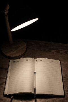 Open blank notebook on wooden desk under lamp light.