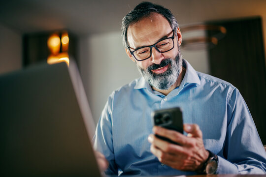 Mature man working remote using smartphone and laptop
