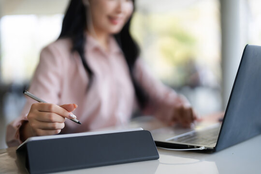 Asian adult professional woman focused working remote office using laptop computer digital stylus tablet for online business creative project