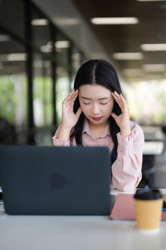 Asian adult woman experiencing work related stress headache burnout deep thought from laptop computer screen fatigue mental pressure study work outdoor modern office campus