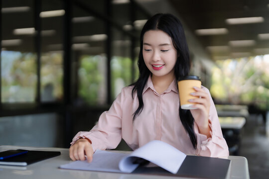 Asian young adult woman studying reviewing notes enjoying coffee working remotely learning new skill student researcher business education finance planning outdoors cafe setting