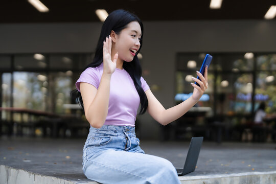 Young Asian woman video calling smartphone outdoor campus setting communicate study work remote connect online lifestyle