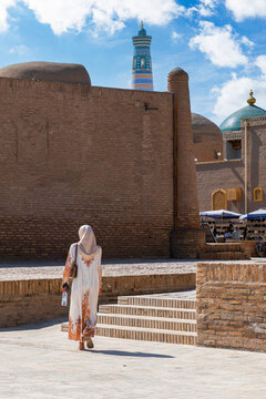 Khiva, Khorezm Province, Uzbekistan - May 31, 2025: Rear view of a Muslim woman in a hijab walking down the stone steps by the ancient brick walls of Itchan Kala