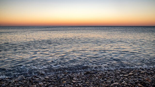 Pebble beach and calm Mediterranean sea at sunset in Kato Zakros on southern coast of Crete Greece with orange evening sky