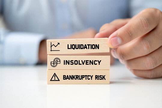 Hand stacks wooden blocks with financial terms liquidation insolvency and bankruptcy risk signifying business challenges and financial peril