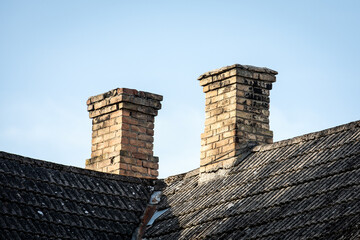 Two Brick Chimneys on Old Corrugated Roof Against Clear Blue Sky