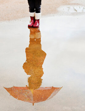 Close-up of a girl in wellies standing in a puddle and her full Reflection holding an umbrella