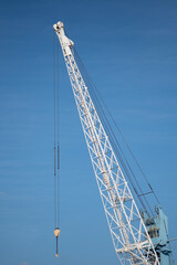 Fototapeta premium Industrial crane with blue sky background. Old, weathered metal structure. The glass control cabin with ladder. Machinery used in shipping ports, cargo terminals. Vertical 