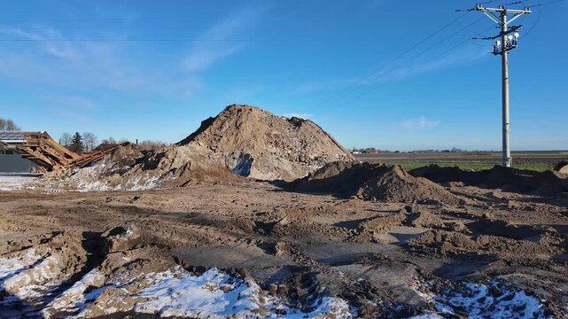 Sand and aggregate piles at a construction site in winter, earthworks with a mobile screening plant, storage of building materials under a clear blue sky, site preparation for infrastructure investmen