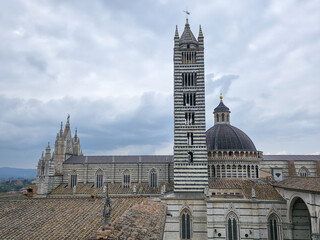 Obraz premium Siena Cathedral with the iconic striped bell tower and dome under a cloudy sky, medieval architecture, Tuscany, Italy