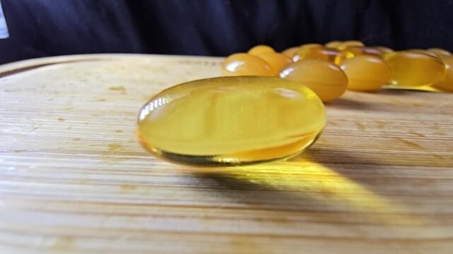 Macro shot of a golden fish oil capsule with soft lighting on a wooden surface, highlighting purity and health.