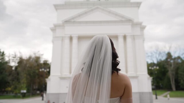 Bride in wedding dress and veil from behind, standing before a grand white classical building, symbolizing new beginnings