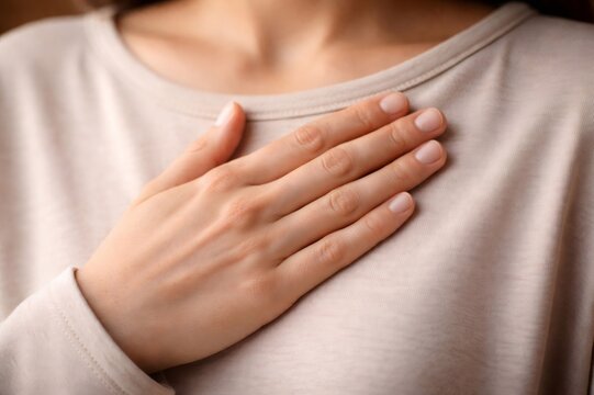 Woman placing hand over her chest in a gentle, sincere gesture conveying gratitude, honesty, self love and compassion, close up on emotion, calm and peaceful wellbeing