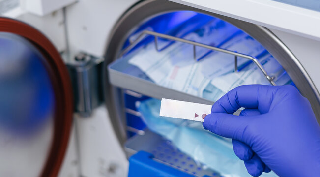 Gloved hand loading dental autoclave with sterilized instrument pouches and indicator strip for sterilization procedure background and instructional poster