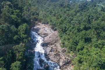 Wild waterfall stream cascading among lush green jungle trees with distant cable car gondola © Alexandre Arocas