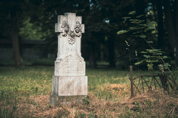 Stary, kamienny nagrobek z ozdobnym motywem roślinnym na trawiastym cmentarzu. Nastrojowe ujęcie zabytkowej steli w otoczeniu natury i zieleni. Symbol pamięci. © Henryk Niestrój