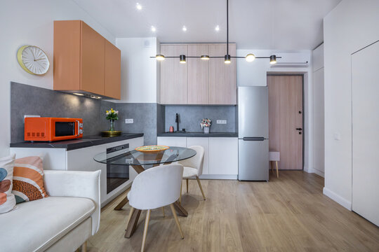 A cozy kitchen and dining space shows a table with chairs, a microwave, and a refrigerator. Sunlight fills the area, creating a welcoming atmosphere in this apartment
