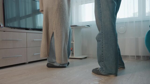CloseUp Floor Feet Showing Two People Standing In Living Room, Partners Frozen In Awkward Pause Near Sofa, Slippers And Denim Visible, Soft Window Light, Subdued Domestic Tension And Intimate