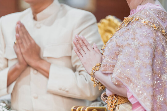 The bride and groom sit putting their hands together in a prayer position and dress in Traditional Thai Costumes.Thai traditional wedding ceremony.