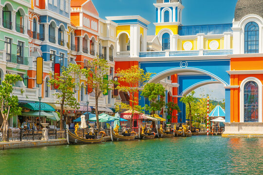 Colorful Mediterranean style buildings and gondolas along peaceful canal on Phu Quoc island, Vietnam. Resort promenade with cafes, trees and bright facades in coastal tourist district