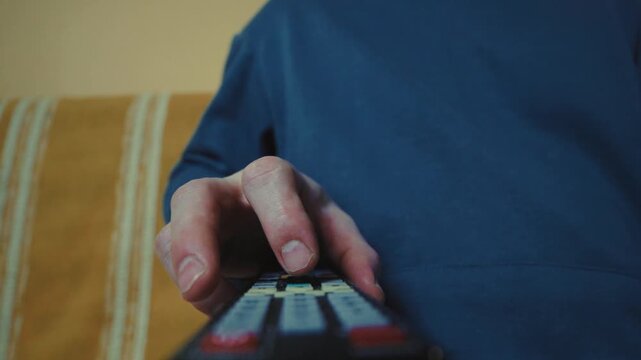 Close up of a hand clicking buttons on a TV remote control to change channels.