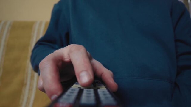 Close up of a hand clicking buttons on a TV remote control to change channels.