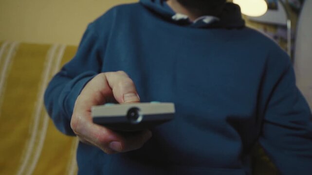 Close up of a hand clicking buttons on a TV remote control to change channels.