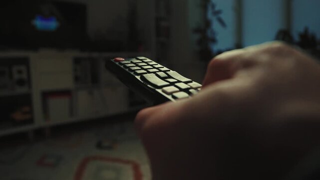 Close up of a hand clicking buttons on a TV remote control to change channels.