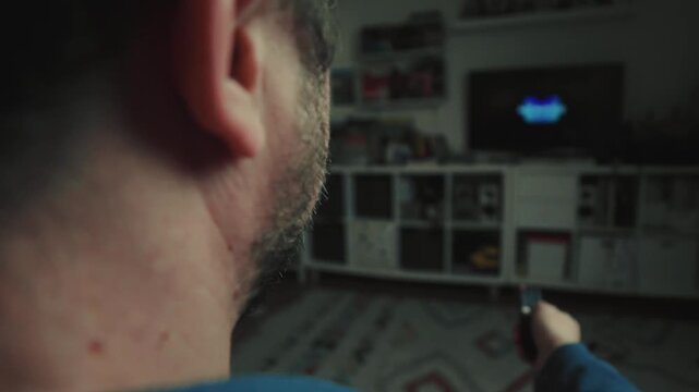 Close up of a hand clicking buttons on a TV remote control to change channels.